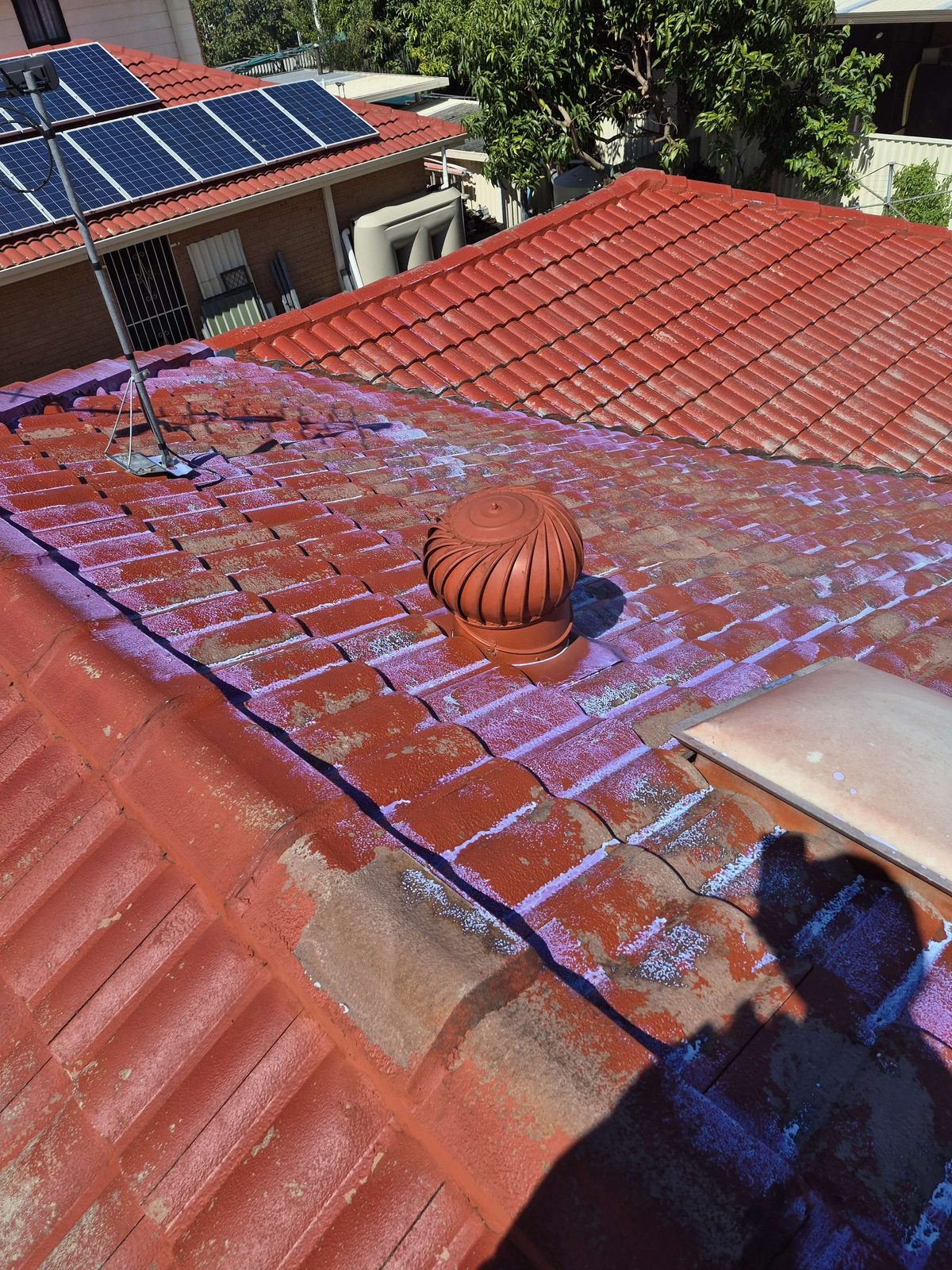 Primer coat being sprayed onto a terracotta tile roof, patchy purple-white basecoat visible